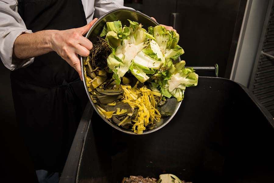 Chef emptying vegetable scraps into a composting bin