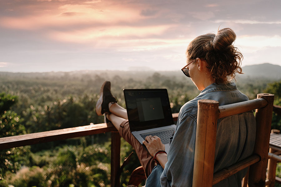 Young Business Woman Working At The Computer In Cafe On The Rock. Young Girl Downshifter Working At A Laptop At Sunset
